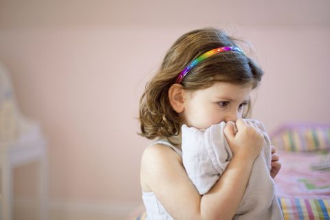 unhappy three year old girl in bedroom holding comfort blanket to face