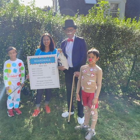the family game night family halloween costume featueres a woman dressed up as a boardwalk card from monopoly, a man dressed as monopoly's uncle pennybags, a boy dressed as the operation game board and another boy dressed as the twister game board