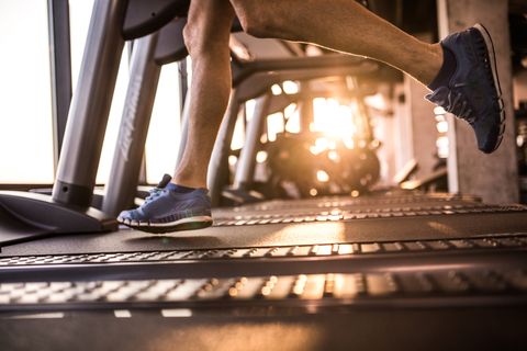 Unrecognizable male athlete running on treadmill in health club.