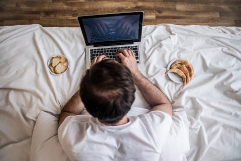 Unrecognizable man working from home using his laptop while enjoying some morning snacks