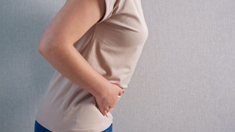 unrecognizable woman holding belly with severe pain, side view