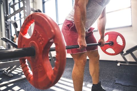 unrecognizable young fit man in gym working out with heavy barbell, doing dead lift
