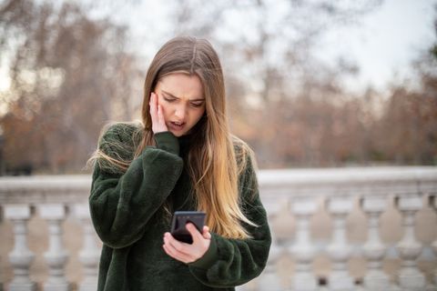 upset young woman using mobile phone while standing in park during winter