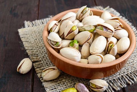 Useful nuts - pistachios in a ceramic bowl on a dark wooden background.