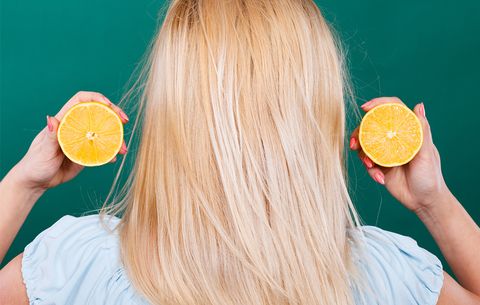woman holding cut lemon near hair