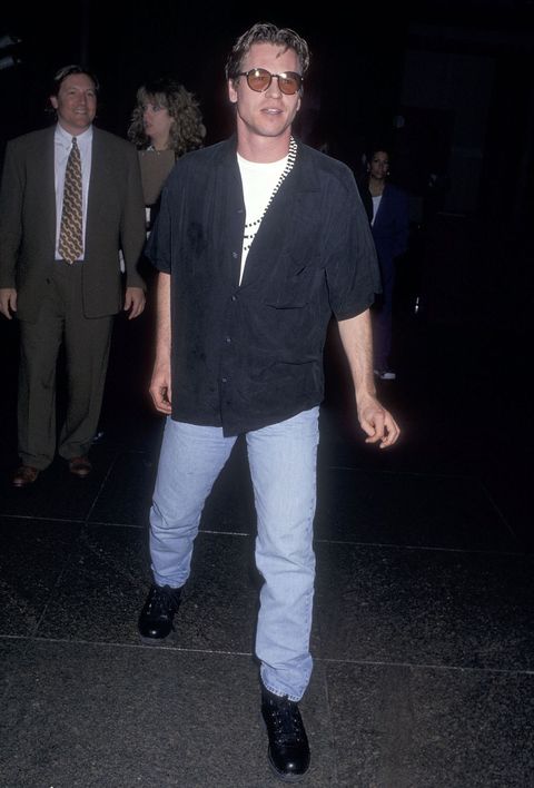 val kilmer en 1995 con camisa de manga corta negra, vaqueros y botas de estilo montañero