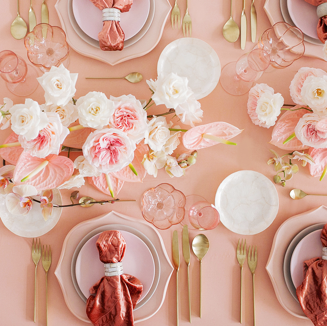 overhead view of pink and white flowers arranged on a pink tablecloth with pink and white dinnerware