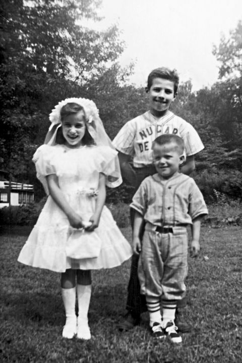 a seven year old valerie wearing her first communion dress stands alongside her brothers joe and jimmy