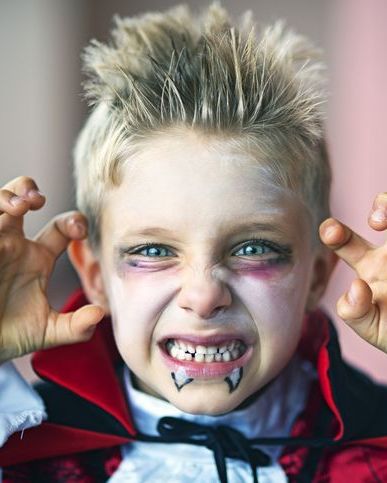 a blonde headed boy with teeth snarled and dressed up like a vampire for halloween