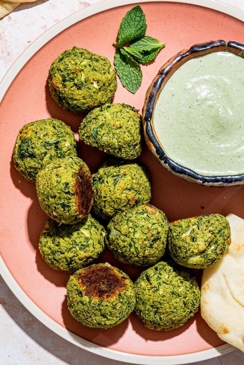 green baked falafel with a bowl of tahini mint dressing and pita on a pink plate