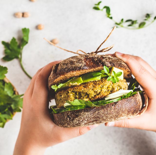 vegan sandwich with chickpea patty, avocado, cucumber and greens in rye bread in children's hands