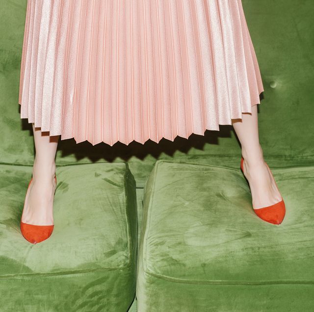 woman with pleated skirt standing on green velvet sofa
