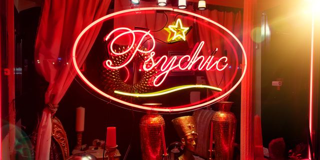 een winkelraam met een rood lichtbord waarop psychic te lezen valt en diverse versieringen