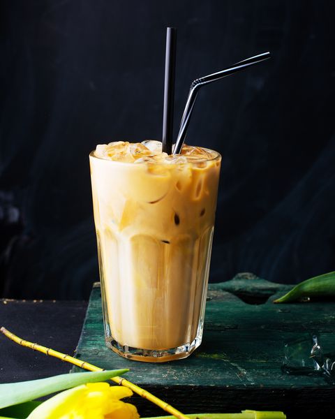 Vertical image of a glass with milk fruit pumpkin, turmeric, cream drink with iced cubes on black background.