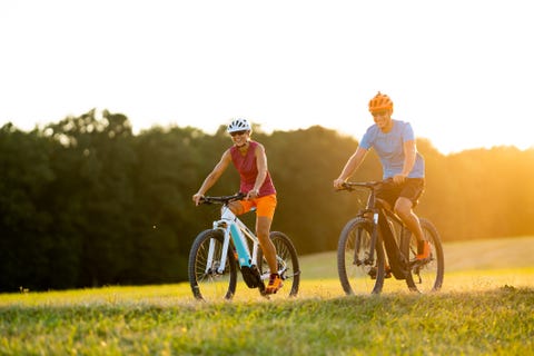 very happy smiling fit sporty couple on e mountain bikes on sunny afternoon in grassland