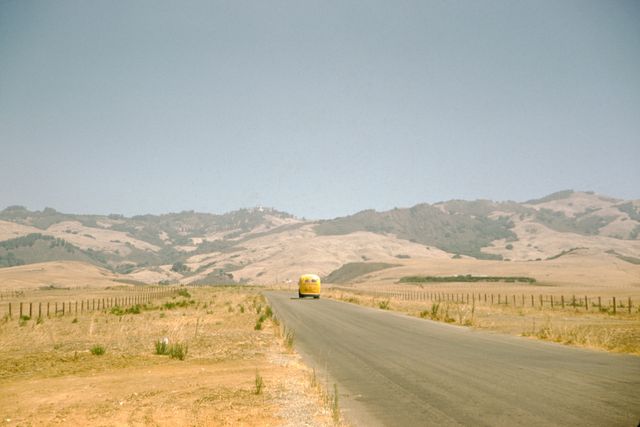 a yellow volkswagen bus travels along a country road that cuts through a prairie covered in dry grass, low rolling hills can be seen in the background, 1960 photo via smith collectiongadogetty images