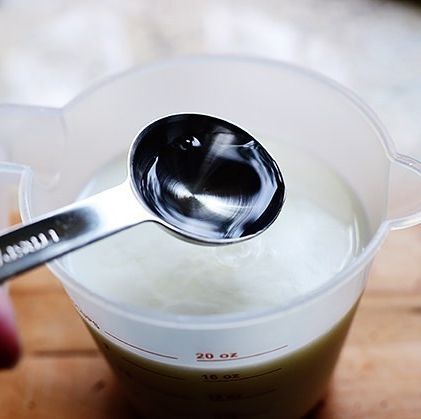 vinegar in measuring spoon with buttermilk in measuring cup