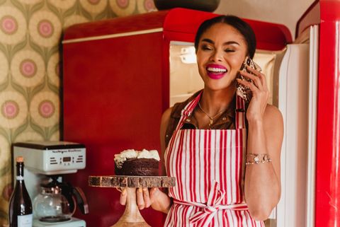 woman on the phone in a white and red striped apron, carrying a cake