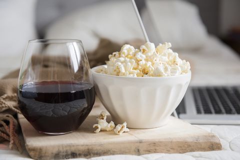 Bowl of popcorn and glass of wine near laptop