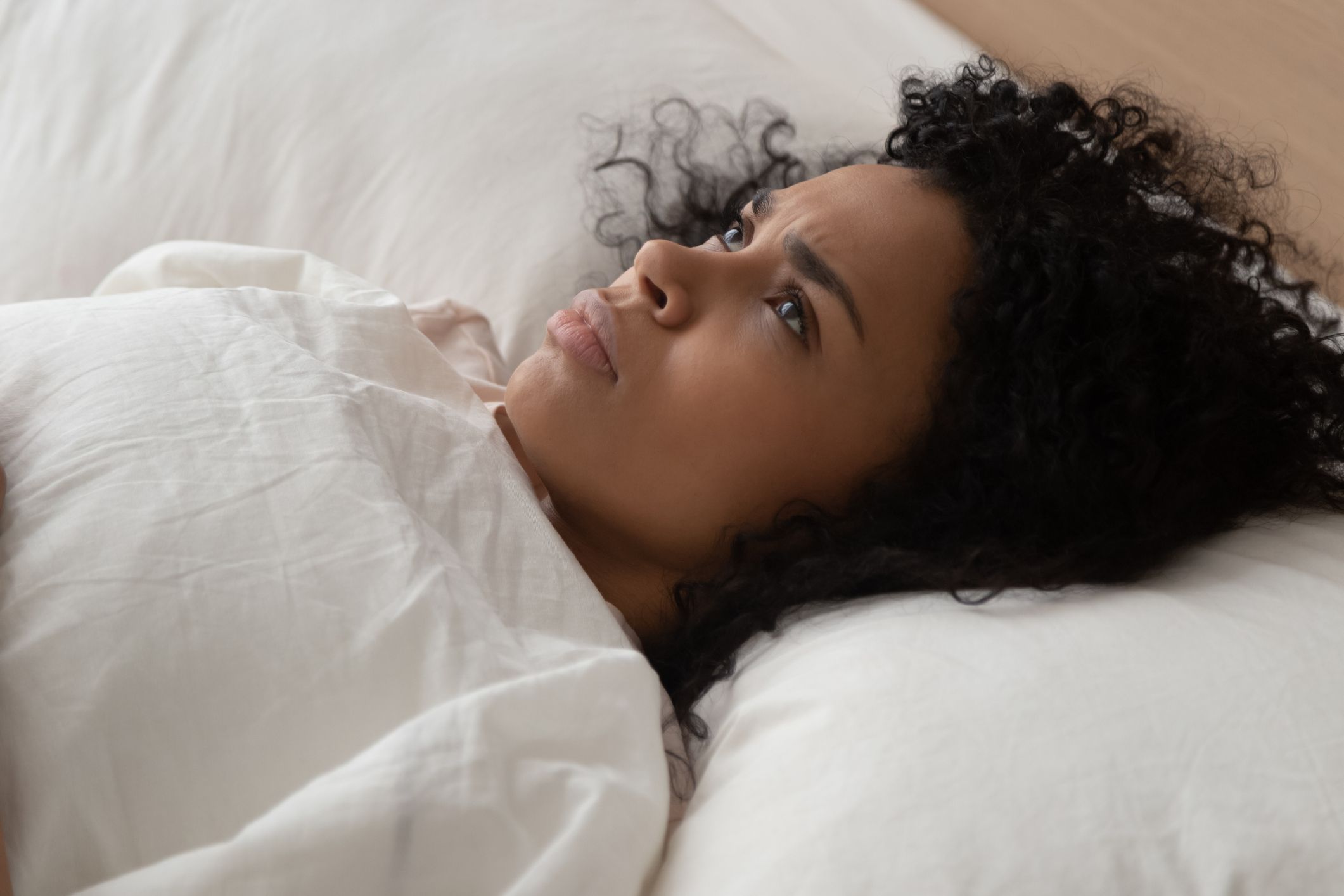 Woman on the bed looking at the ceiling with a pissed off face.