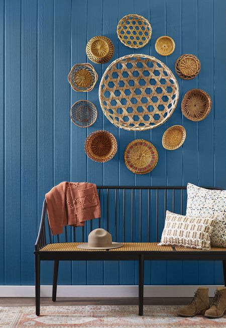 baskets of all styles arranged on a wall that is painted blue with a bench in front of it