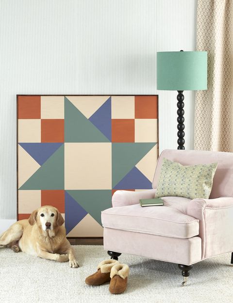 a large piece of artwork in a geometric quitl square shape propped up on a wall by a chair lamp and dog