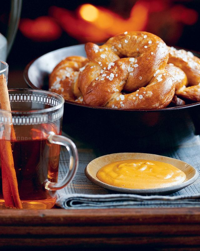 how soft pretzels in a bowl with cheese dipping sauce and cups of spiced cider