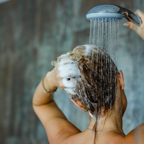 back view of a woman washing her hair with a shampoo in bathroom copy space