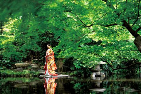 ホテルニューオータニの緑豊かな日本庭園の池のほとりで、きもの姿で立つ新婦の写真