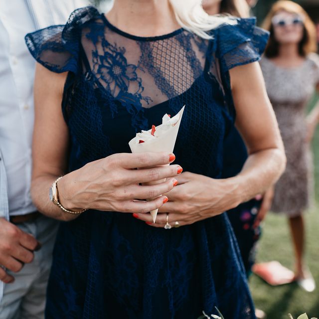 wedding guest in navy lace dress holding confetti