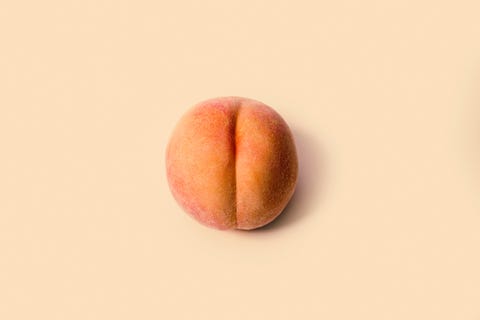 a detailed image of a freshly picked ripe peach  photographed on a peach colored background