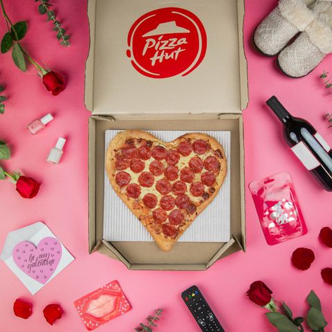 pizza hut heart shaped pizza with pepperoni in open pizza box on a pink background with wine, roses petals, nail polish, valentine's day card