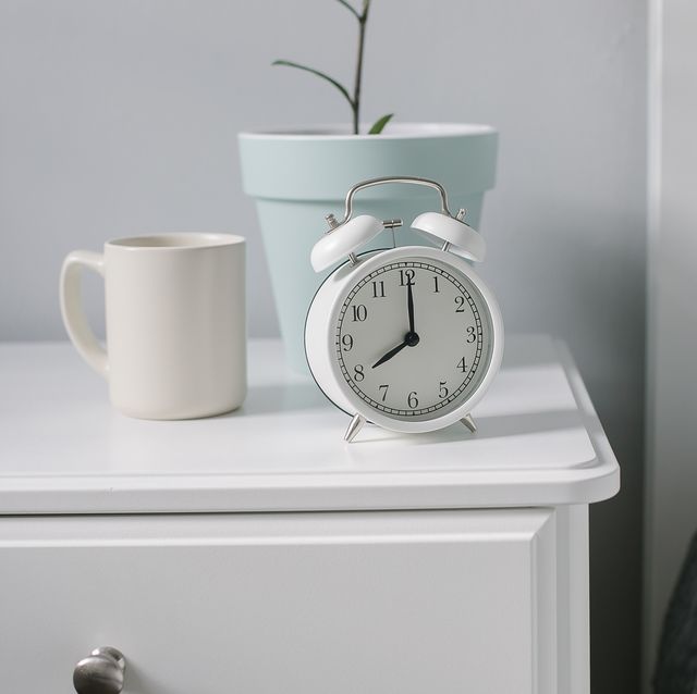 white alarm clock beige cup with coffee tea house plant on bedsite in the bedroom