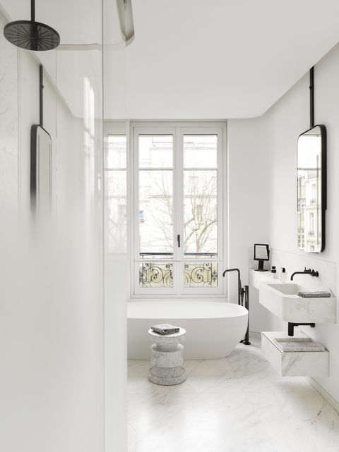 a white bathroom with marble floors and sinks and a soaking tub under the window