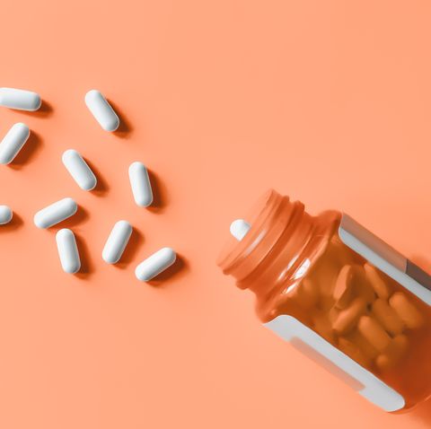 white pills spilling out of prescription bottle onto orange surface