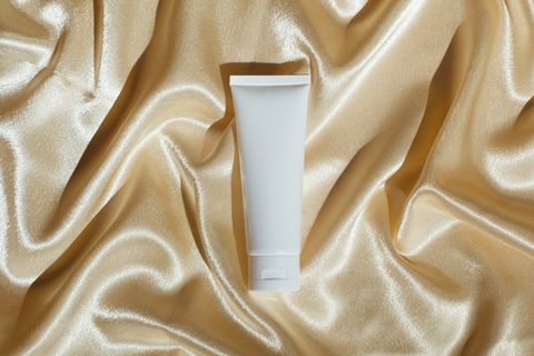 white tube bottle with moisturizer on silk fabric beige background beauty products skin care concept