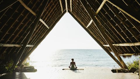 wide shot of woman relaxing after practicing yoga in ocean front pavilion at tropical resort