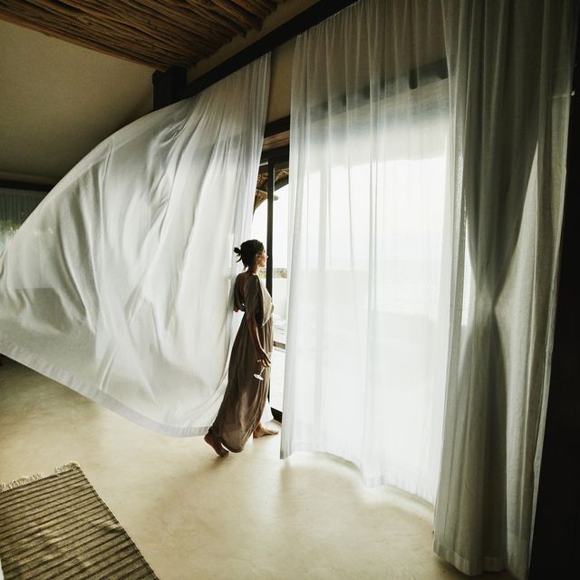 wide shot of woman standing in luxury hotel suite looking at view with curtains blowing in wind