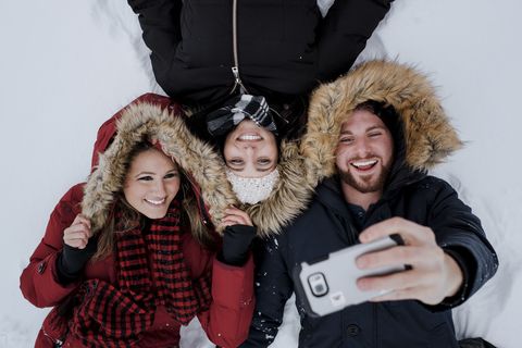 Wide angle friends taking selfie while lying in snow covered field