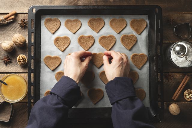 a woman, a young girl or a pastry chef lays out heart shaped cookies on parchment baking paper, on a baking sheet, against the background of a wooden table the concept of cooking, valentine's day