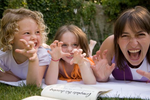 a woman and two girls growling and holding their hands up like claws while lying down in a backyard