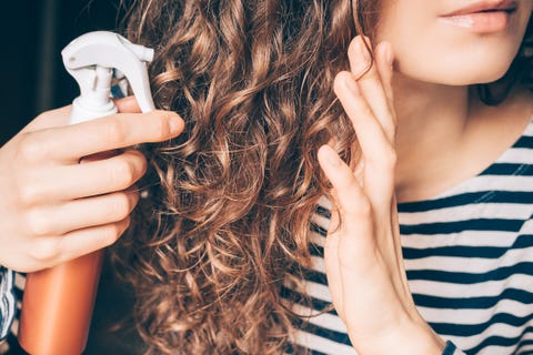 woman applying spray on curly brown hair