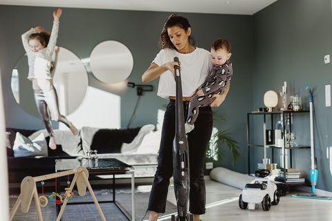 woman carrying toddler and vacuum cleaning room