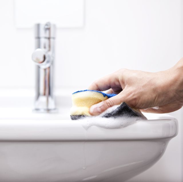 woman cleaning bathroom sink with sponge