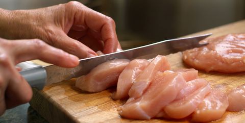 woman cutting raw chicken on a wooden cutting board