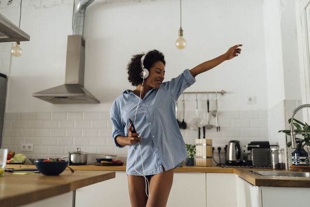 woman dancing and listening music in the morning in her kitchen