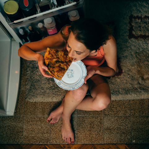 woman eating in front of the refrigerator in the kitchen late night