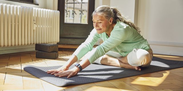woman exercising while sitting on exercise mat over floor in living room