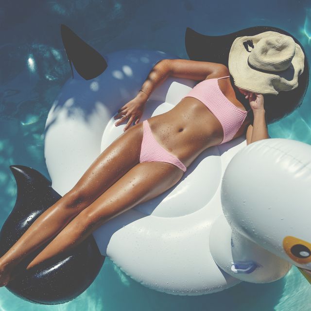 woman floating on a white inflatable in swimming pool in a pink bikini