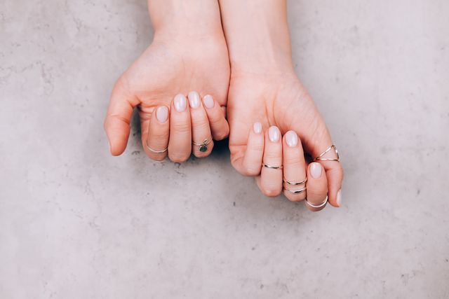 woman hands with nude pink manicure and with many various silver rings on fingers on concrete gray background concept of trendy boho style flat lay style with copy space